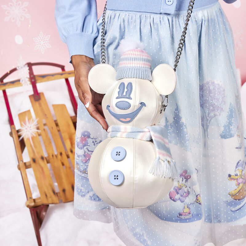 Woman wearing the Mickey Mouse Winter Snowman Crossbody, resting it against the Stitch Shoppe Winter Tulle Overlay Skirt, with a winter background